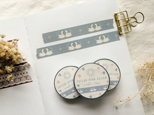 Washi tape rolls showing repeating swans on a light blue background with stars and bows.
